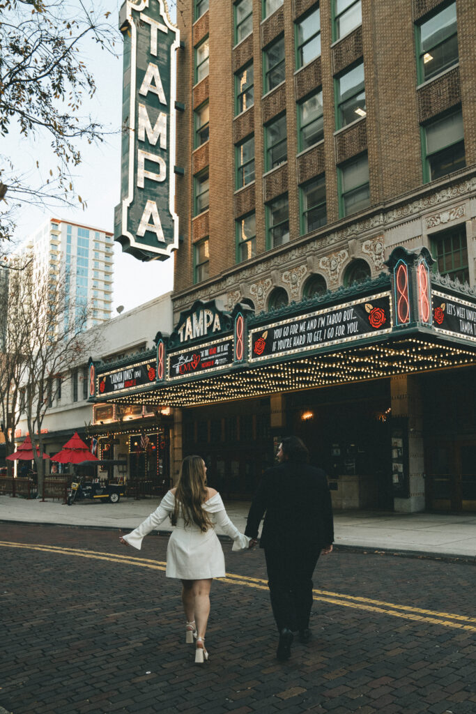 a couple running hand in hand towards the Tampa theatre for a creative engagement photoshoot
