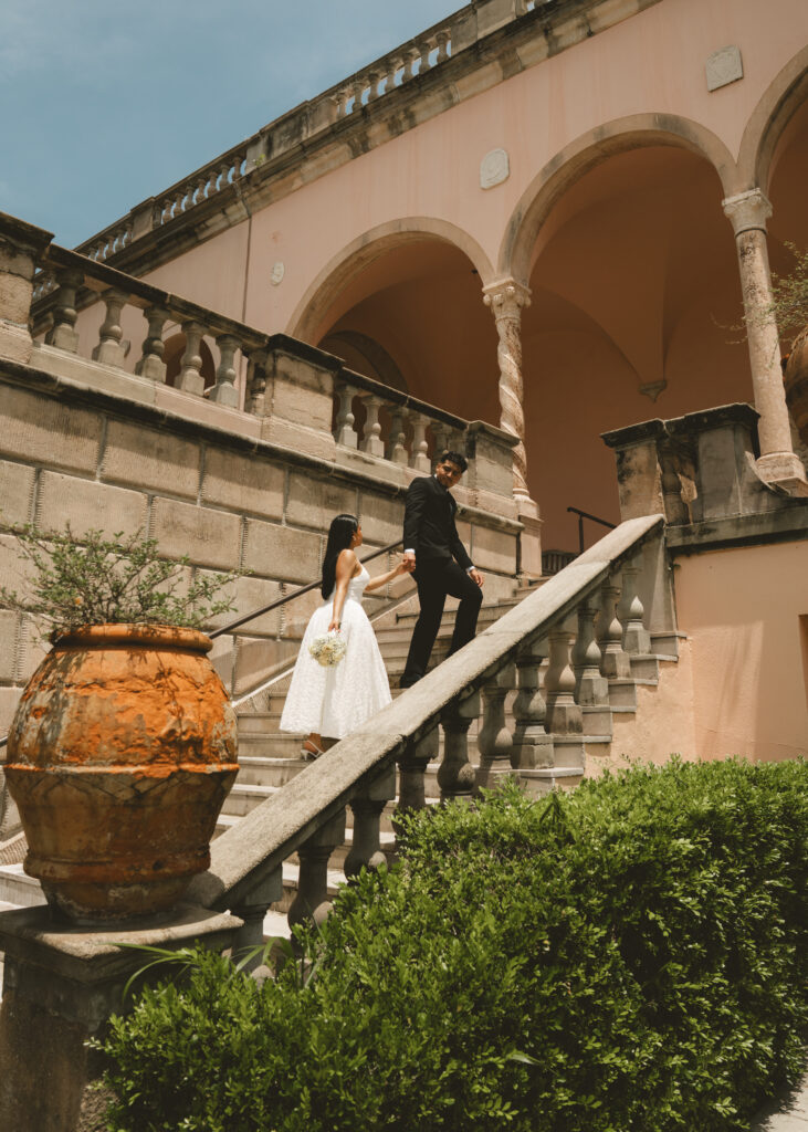 bride and groom walk and in hand up a marble staircase at their engagement session at the Ringling museum