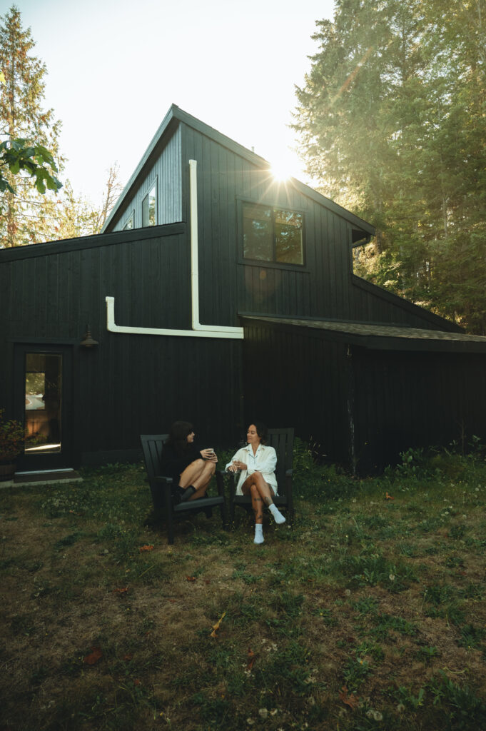 two women having a coffee together outside of a black cabin in Washington