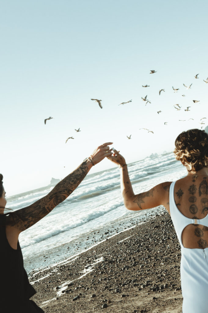 two women running hand-in-hand with seagulls on rialto beach