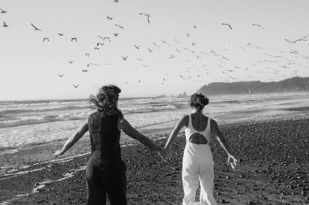 two women running on a beach in Washington with seagulls flying overhead