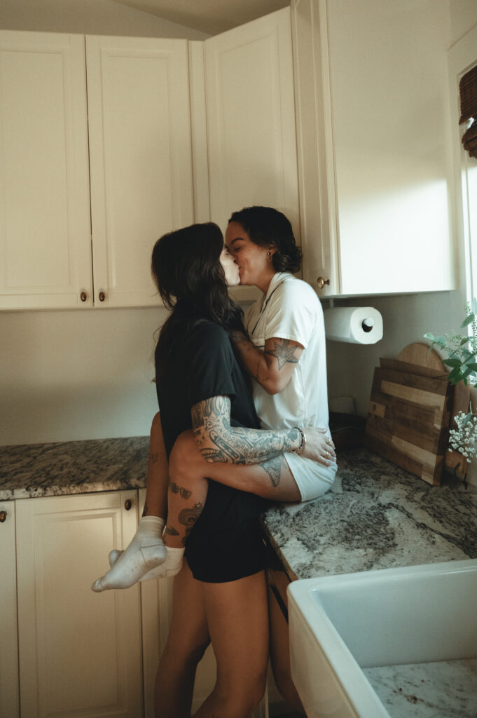 one woman sitting on the counter while her girlfriend kisses her on the morning of their elopement
